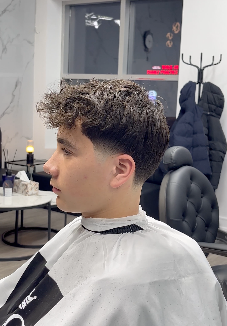 Young person with a faded haircut at a salon, wearing a barber cape.