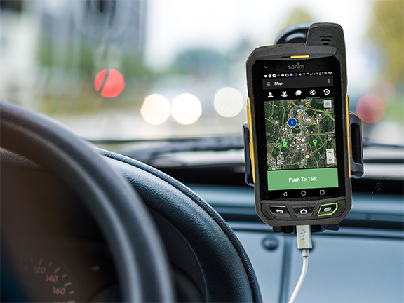 A cell phone is sitting on the steering wheel of a car.