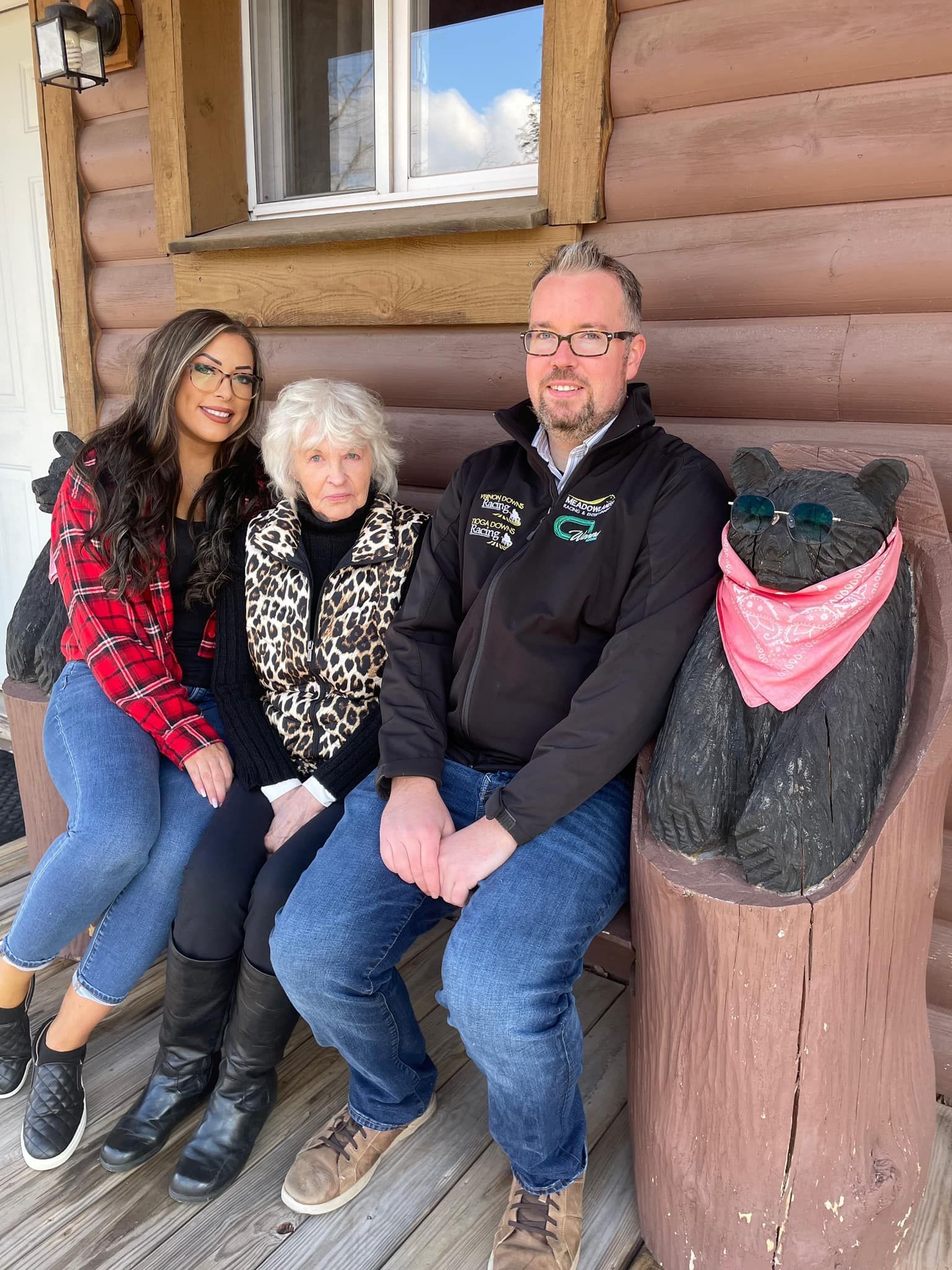 a group of people are sitting on a bench next to a statue of a bear .