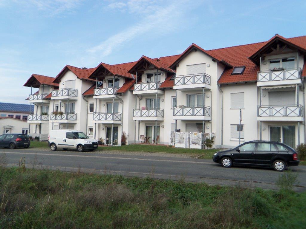 Vor einem großen weißen Gebäude mit rotem Dach parken Autos