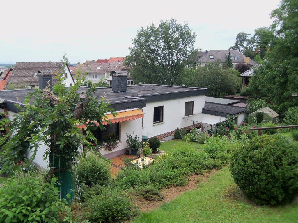 Ein weißes Haus mit schwarzem Dach ist von Bäumen und Büschen umgeben.