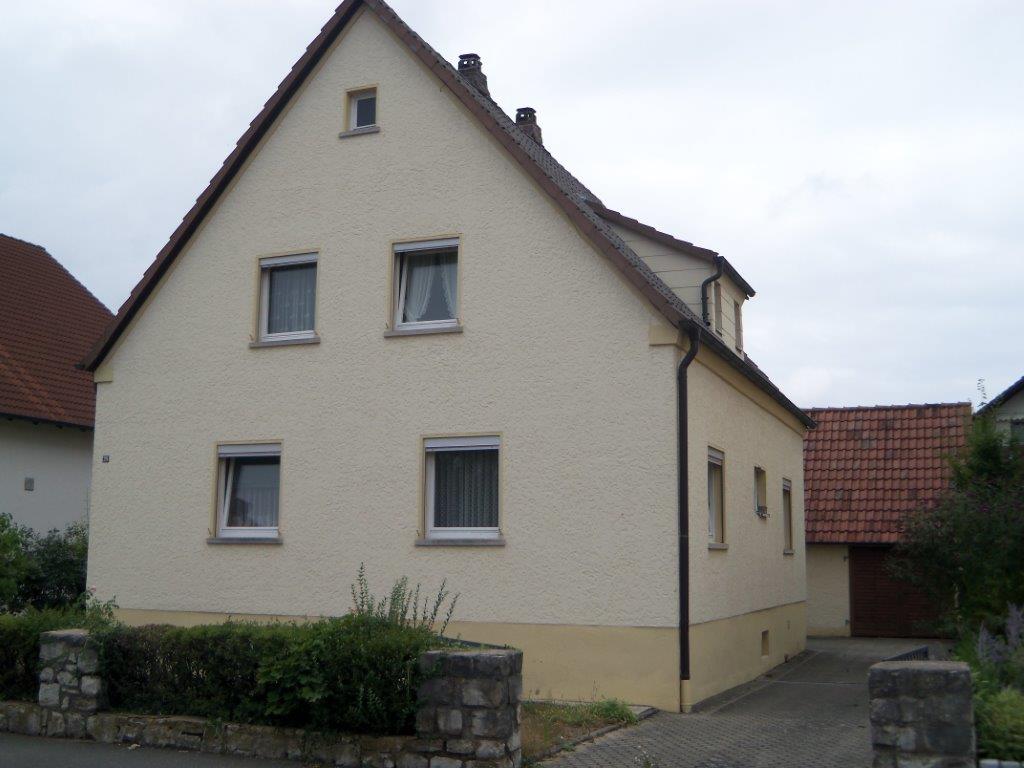 Ein weißes Haus mit drei Fenstern und einem braunen Dach