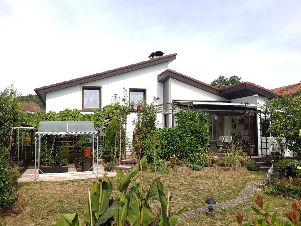 Ein großes weißes Haus mit einem roten Ziegeldach ist von einem üppigen grünen Garten umgeben.