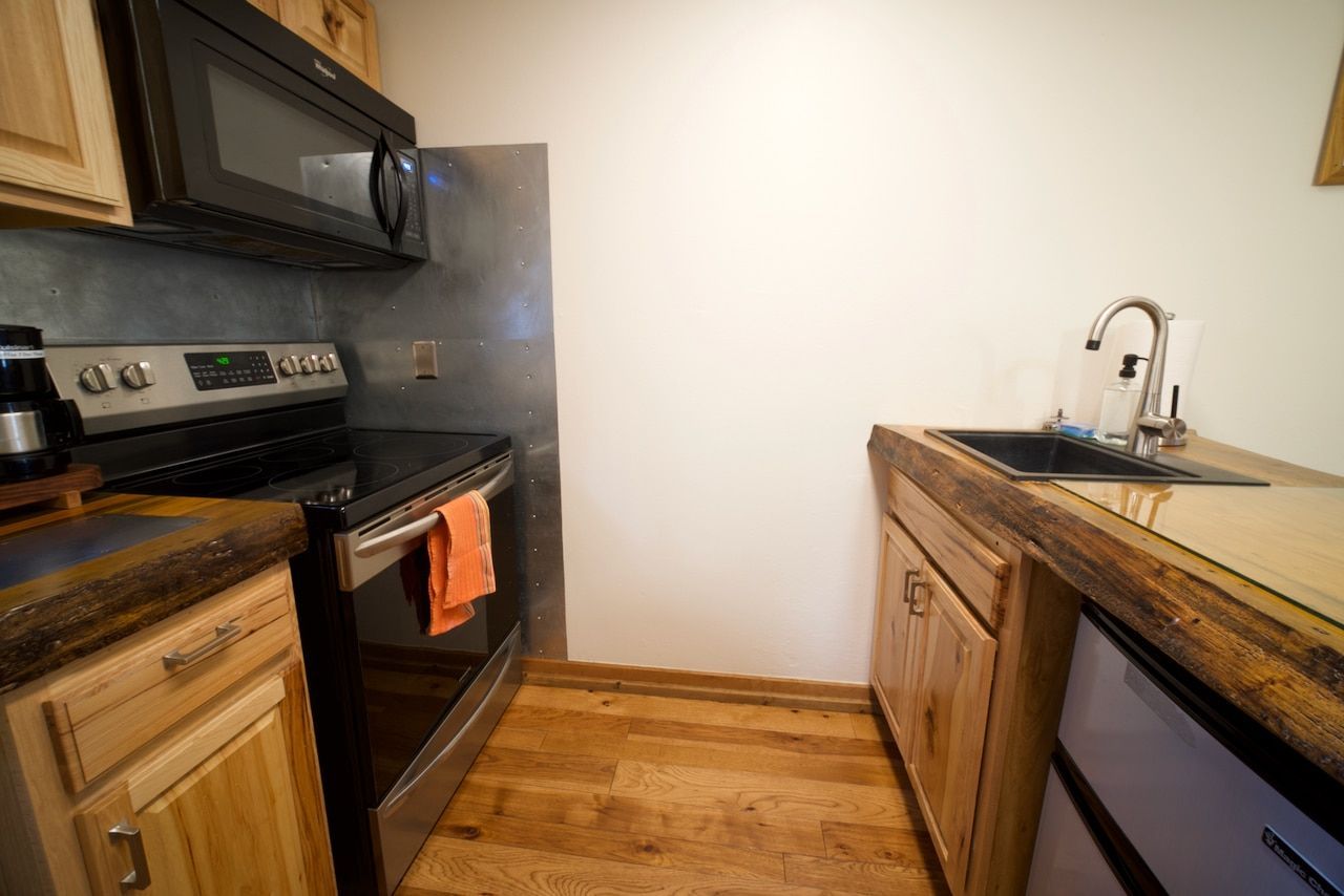 A kitchen with a stove , microwave , sink and wooden cabinets.