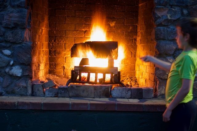A young boy is standing in front of a fireplace.