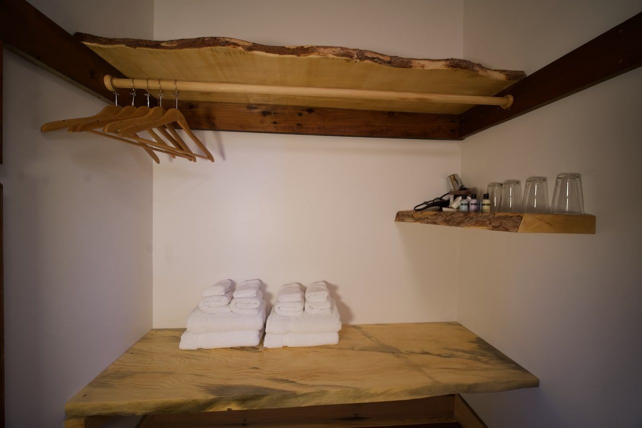 A wooden shelf with towels and glasses on it in a closet.