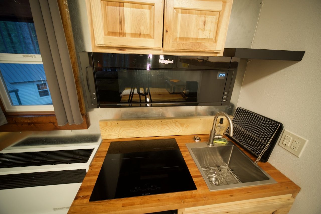 A kitchen with a stove , sink , microwave and a window.