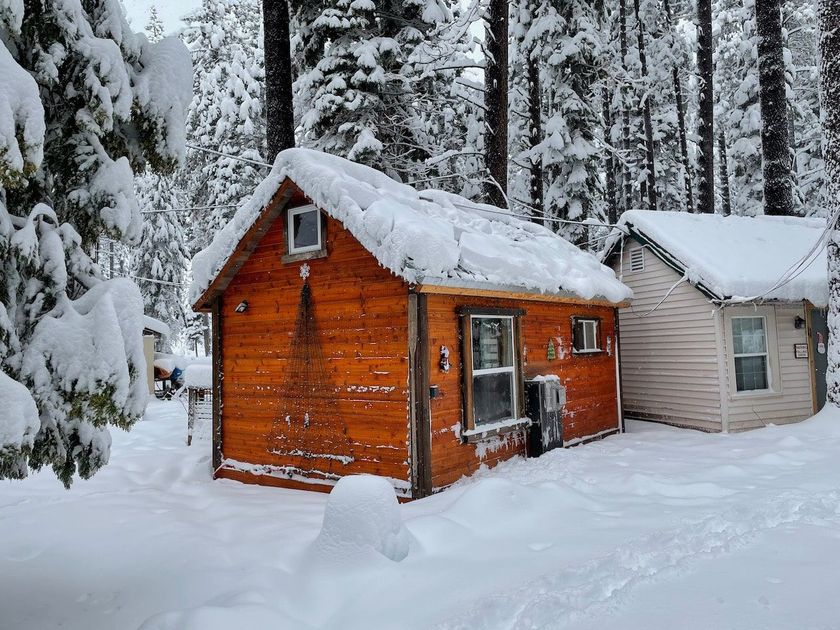 Two small houses are covered in snow in the woods.