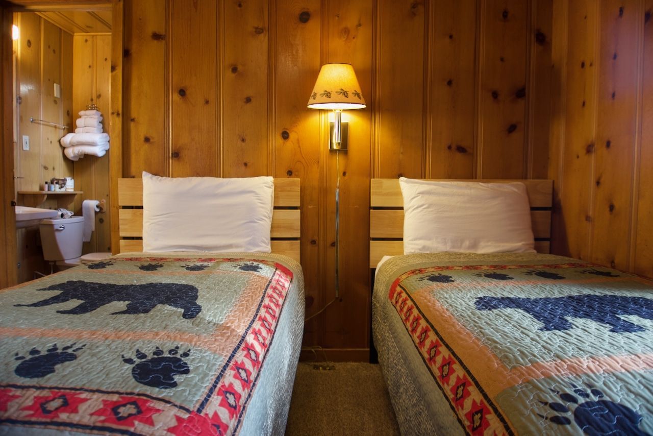 A bedroom with two beds and a lamp on the wall.