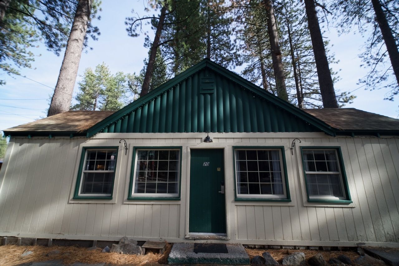 A small white house with a green roof is surrounded by trees