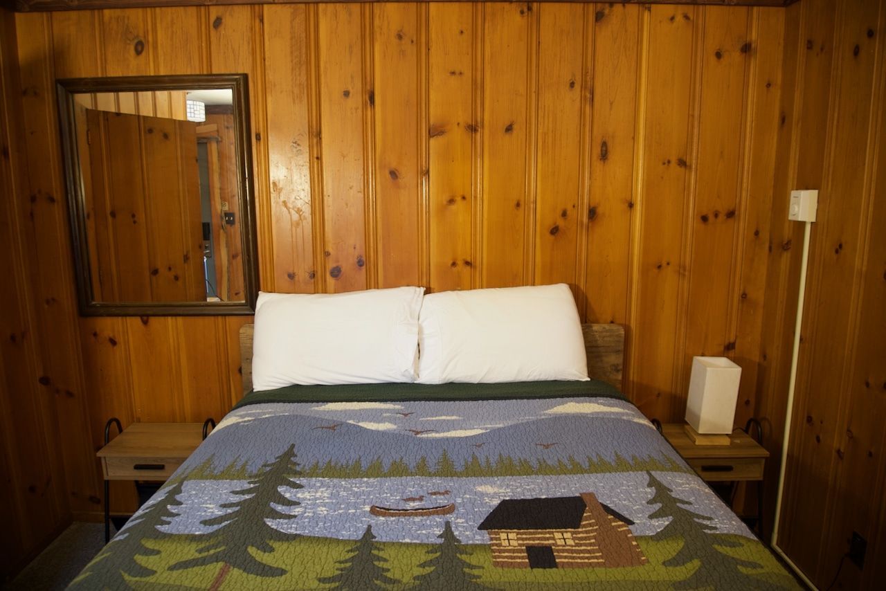 A bedroom with a bed , nightstand , mirror and wood paneling.