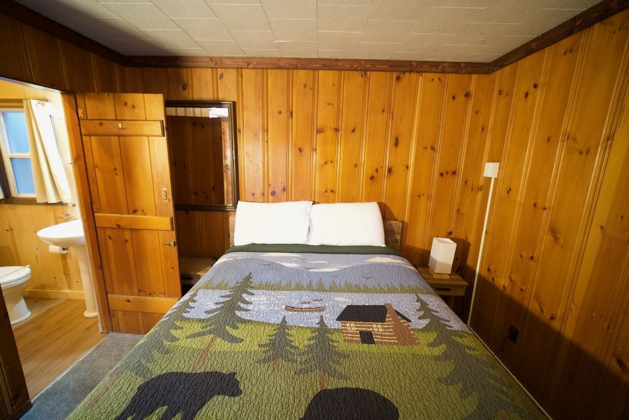 A bedroom with wood paneling and a bed with a bear blanket on it.