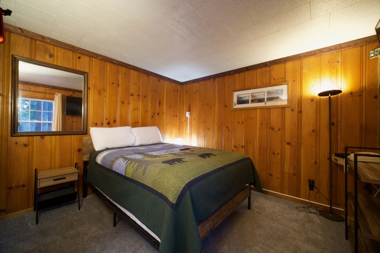 A bedroom with a bed , nightstand , lamp and mirror.