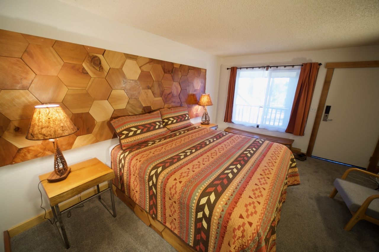 A hotel room with a bed , lamps , and a wooden wall.