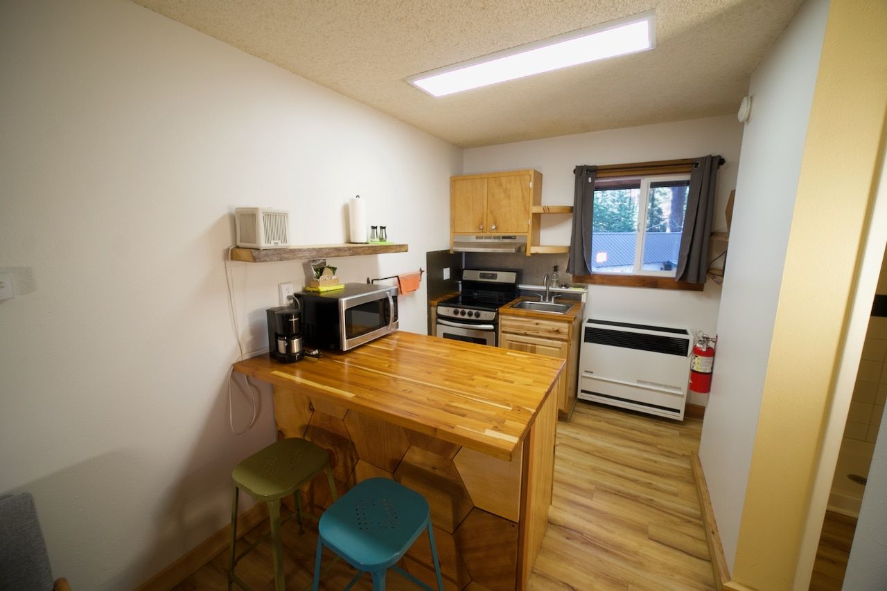 A kitchen with a wooden table , stools , and a microwave.