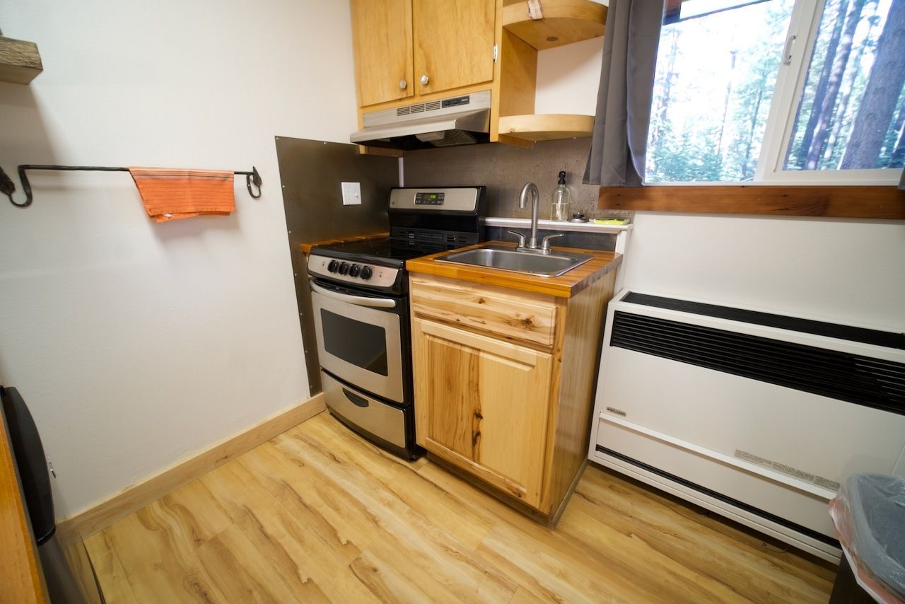 A kitchen with wooden cabinets , a stove , a sink , and a window.