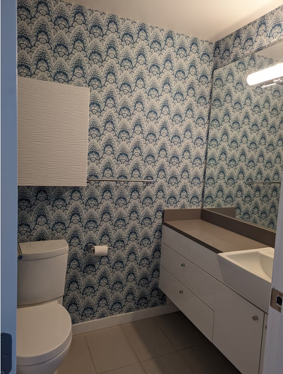 Small modern bathroom with blue patterned wallpaper, white toilet, and white vanity with sink.