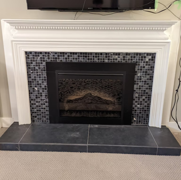 White fireplace with black tile surround and slate hearth beneath a mounted TV