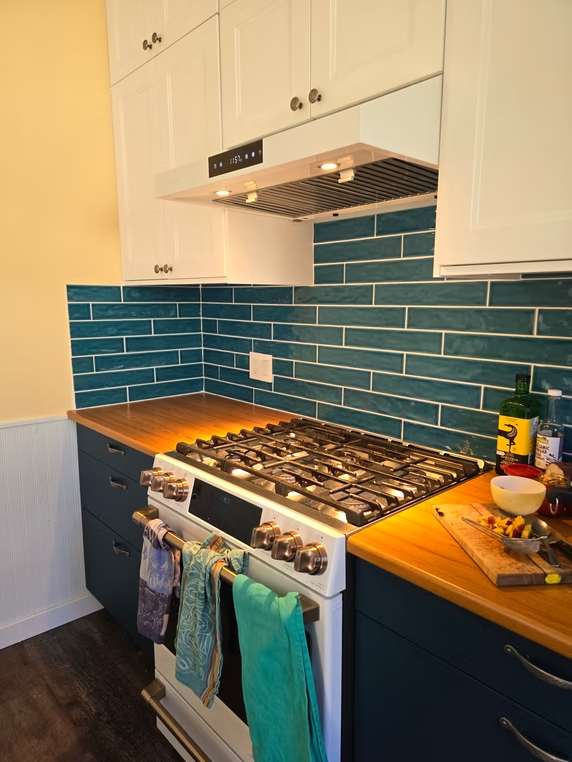 Modern kitchen with blue tile backsplash, white cabinets, and a stainless gas stove with towels hanging on the oven door