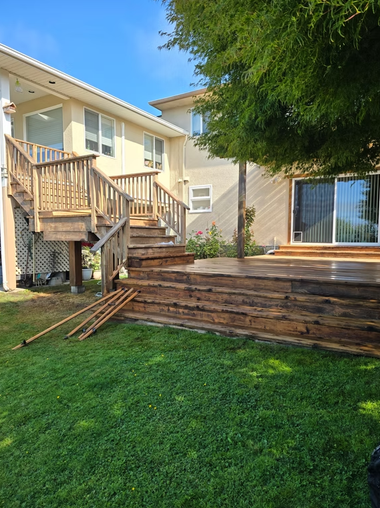 Backyard with wooden deck stairs, retaining wall, and green lawn beside a beige house