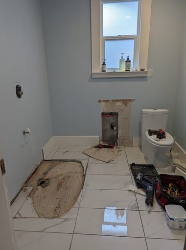 Renovated bathroom under construction with exposed subfloor, toilet, and tools on the floor