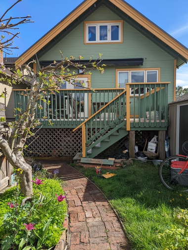 Backyard with green house, raised deck, brick path, lawn, and blooming tree in spring light