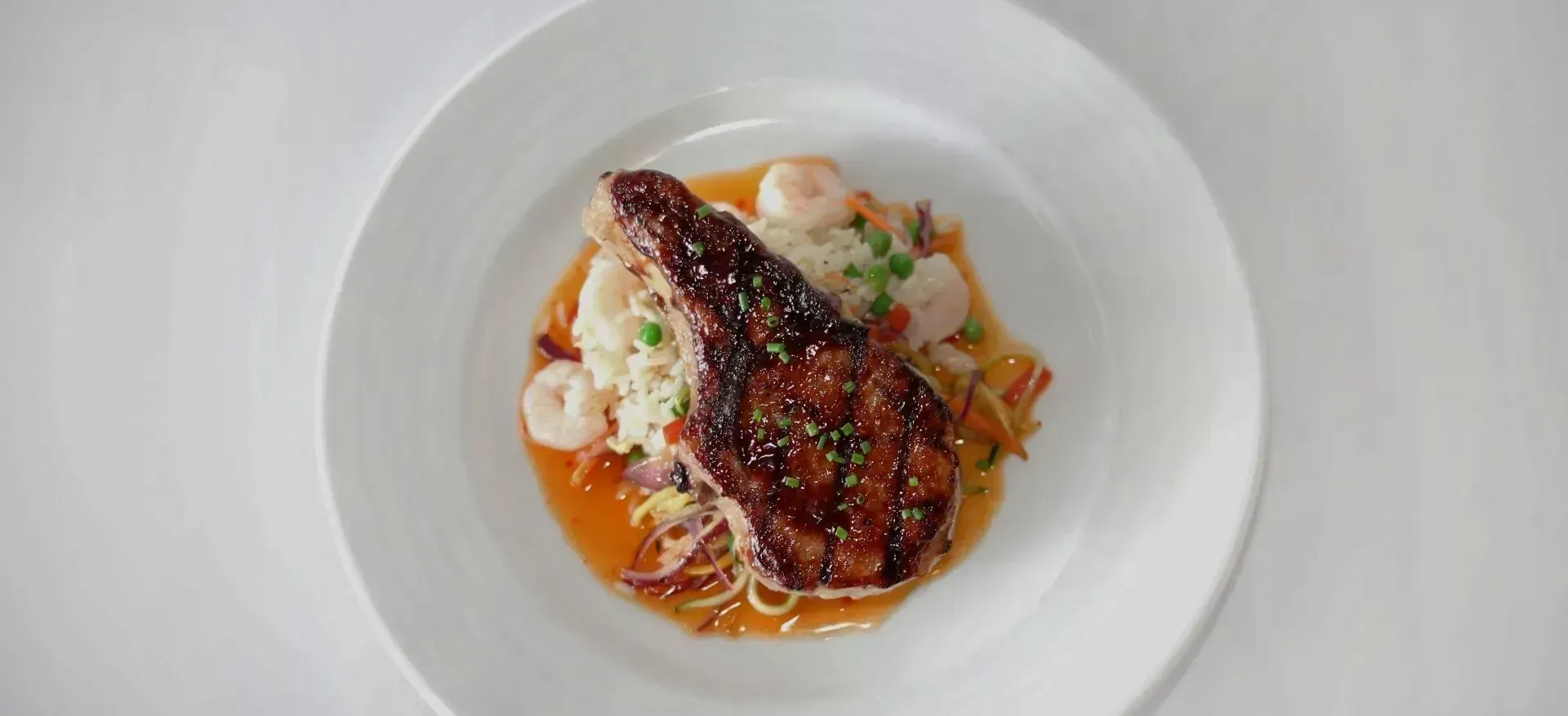 A white plate topped with meat and shrimp on a table.