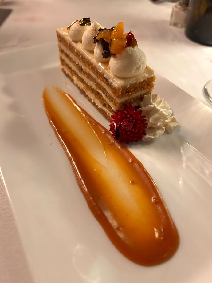 A slice of cheesecake on a white plate with a glass of orange juice in the background.