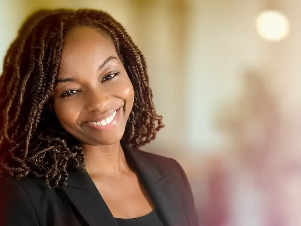 Smiling person with curly hair in a black blazer against a softly blurred background