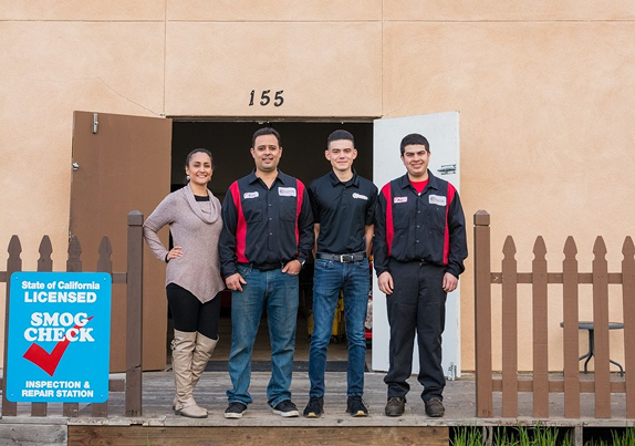 Four people stand in front of an auto repair shop. A 