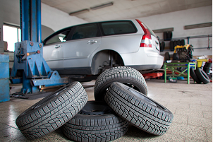 Car on a lift in a garage; four tires piled in the foreground, ready for replacement | Allegiance Automotive