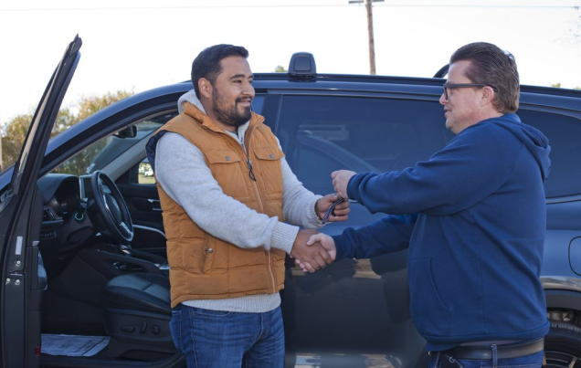 Two men shaking hands next to a dark SUV; one holds keys. Outdoors, sunny | Allegiance Automotive