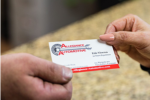 Hands exchanging a business card for Allegiance Automotive. The card has the company logo and contact information | Allegiance Automotive