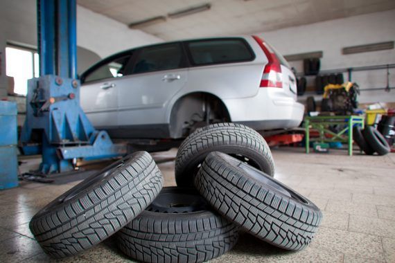 Car in a repair shop with a set of tires in front. Vehicle is raised on a lift | Allegiance Automotive