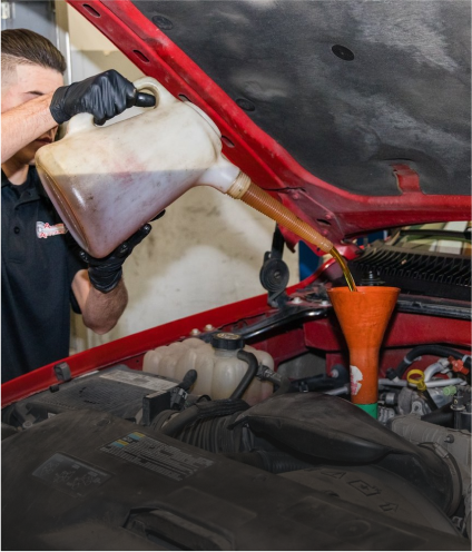Mechanic pouring oil into a car engine using a funnel, red car hood open | Allegiance Automotive
