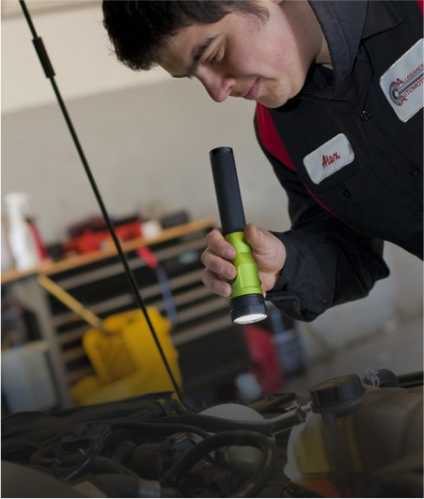 Mechanic inspecting car engine with a flashlight. Garage setting. Dark hair, work uniform, focused expression | Allegiance Automotive
