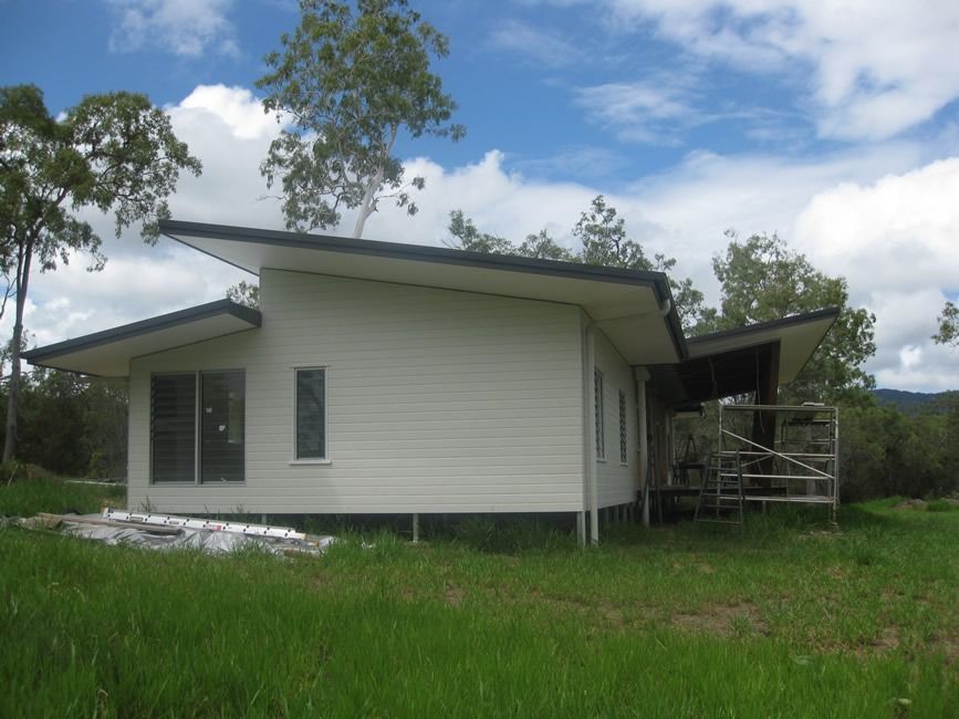 A Small White House Sits In The Middle Of A Grassy Field — Sven Margraf Constructions Pty Ltd In Atherton QLD