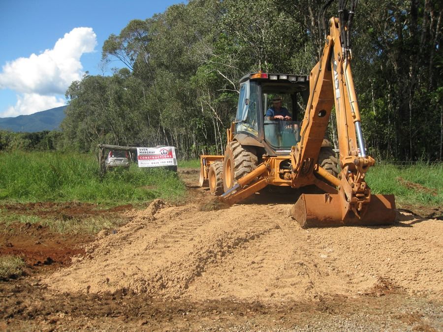 A Man Is Driving A Case Backhoe On A Dirt Road — Sven Margraf Constructions Pty Ltd In Atherton QLD