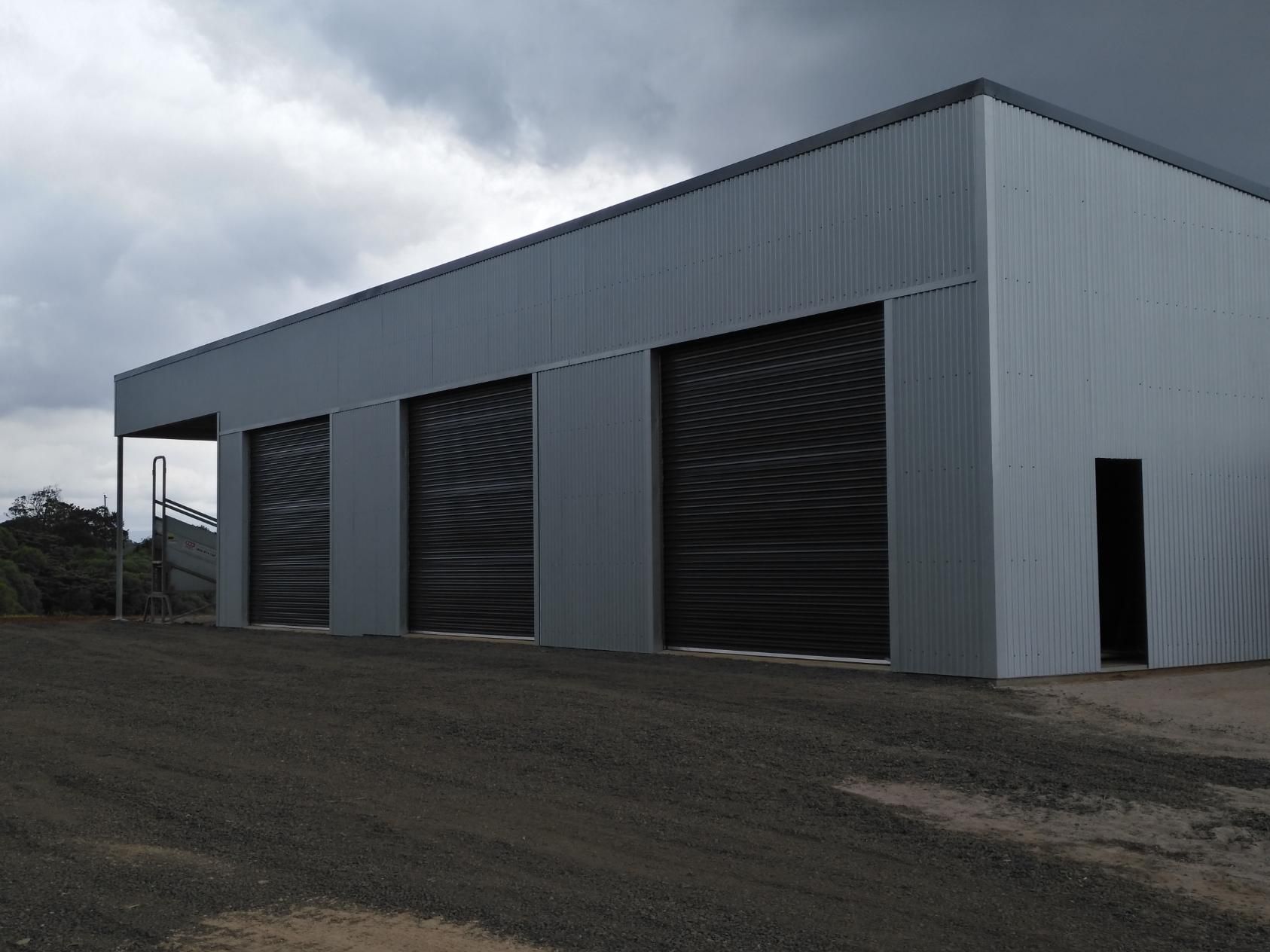 A Large Gray Building With Black Garage Doors On A Cloudy Day — Sven Margraf Constructions Pty Ltd In Atherton QLD