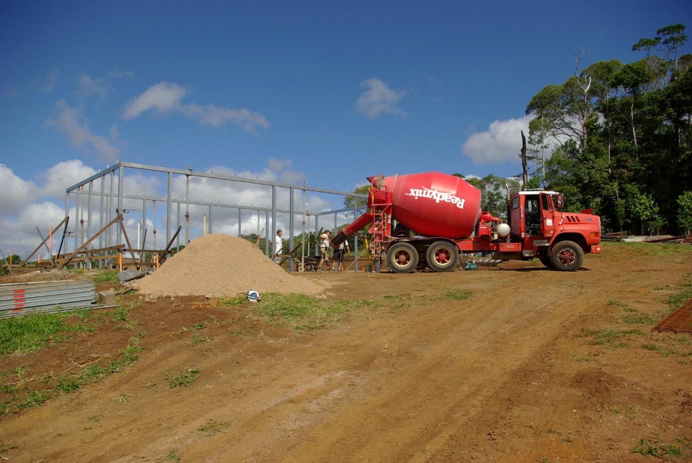 A Red Concrete Mixer Truck Is Driving Down A Dirt Road — Sven Margraf Constructions Pty Ltd In Atherton QLD