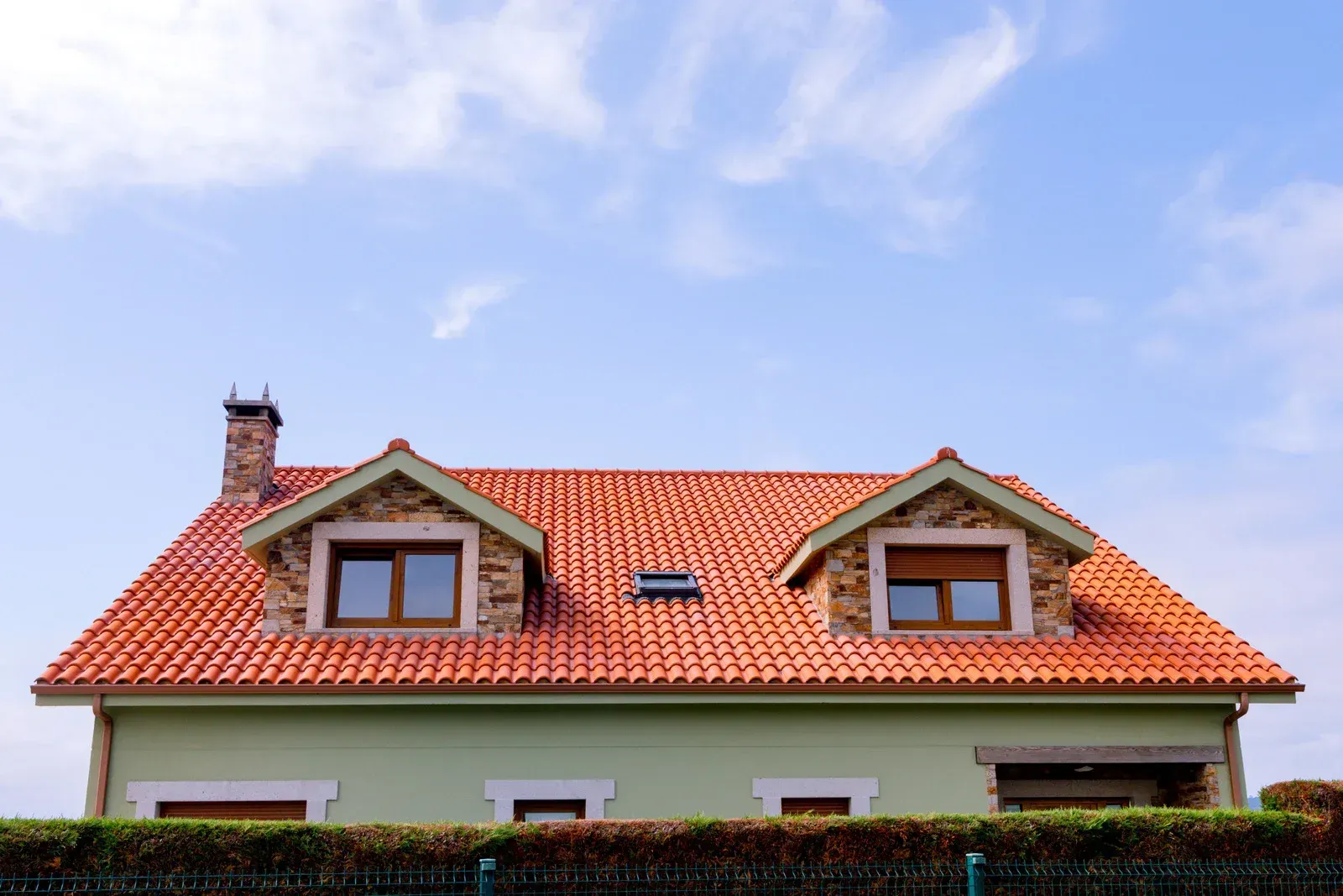 Green house with orange tile roof and two dormers against a blue sky.