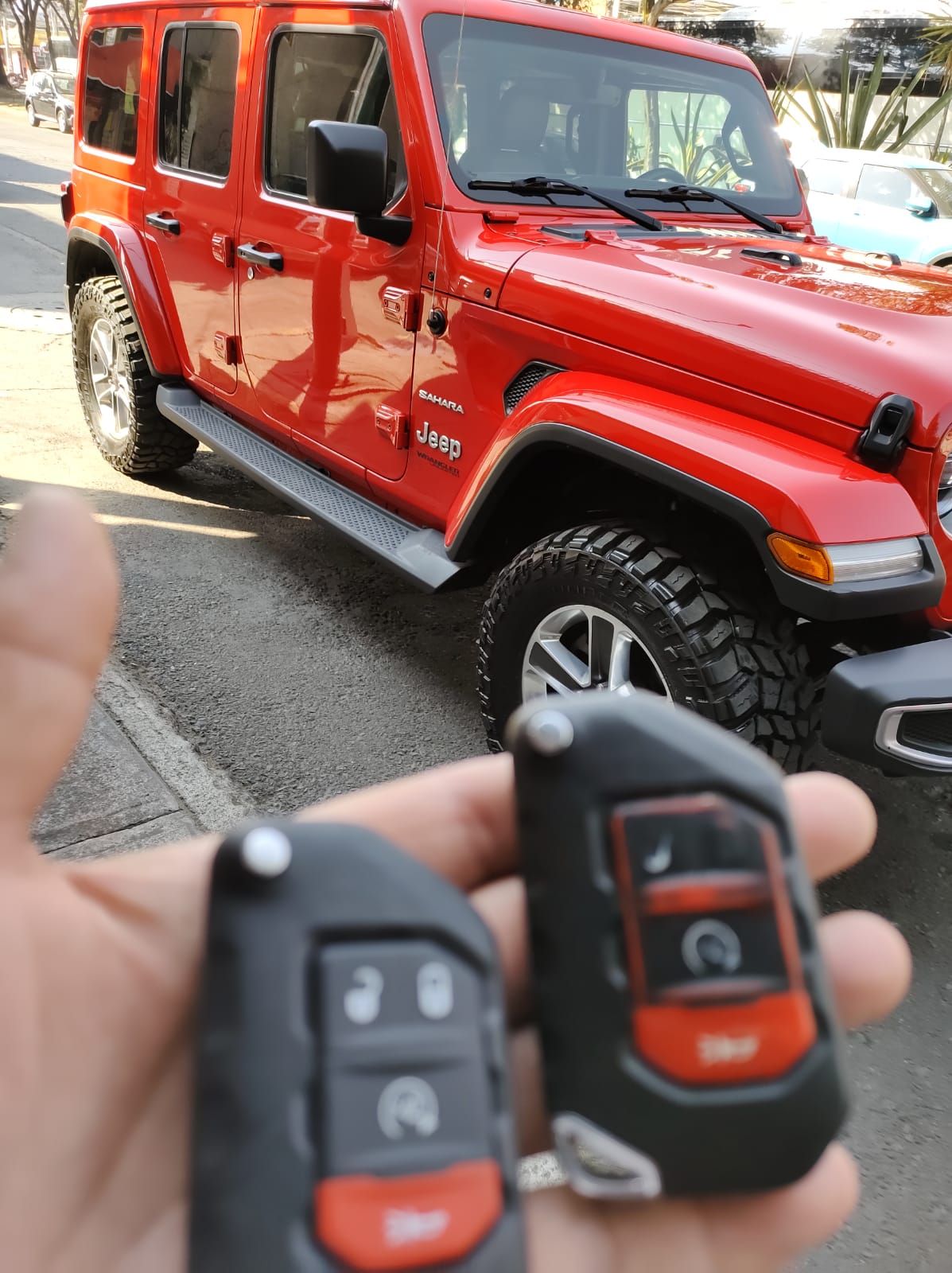 Una persona sostiene un control remoto delante de un jeep rojo.