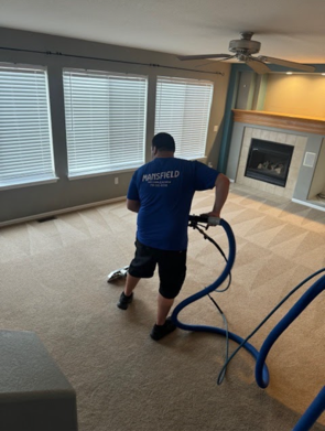 A man in a blue shirt is cleaning a carpet in a living room
