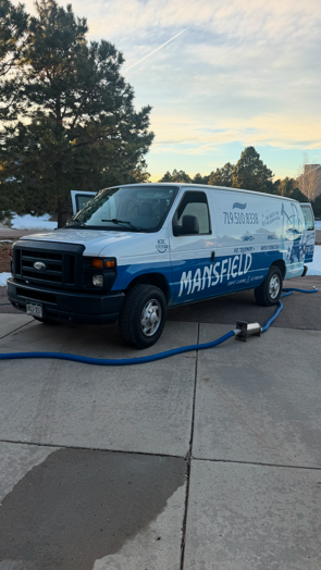 A mansfield van is parked in a driveway with a hose attached to it.