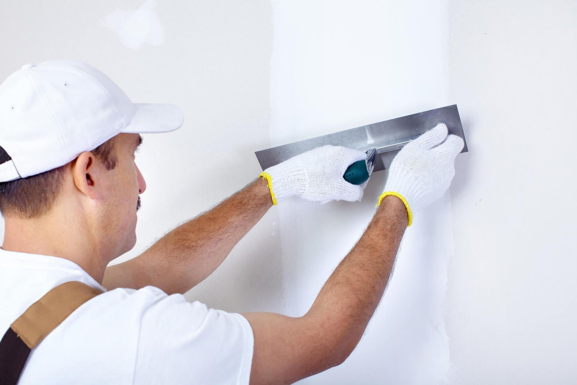 Person in a white cap and gloves smoothing wall with a trowel.
