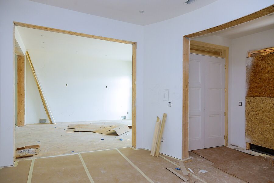 Interior of a room under construction with door and doorway frames. White walls, wood trim, and a partially finished floor.