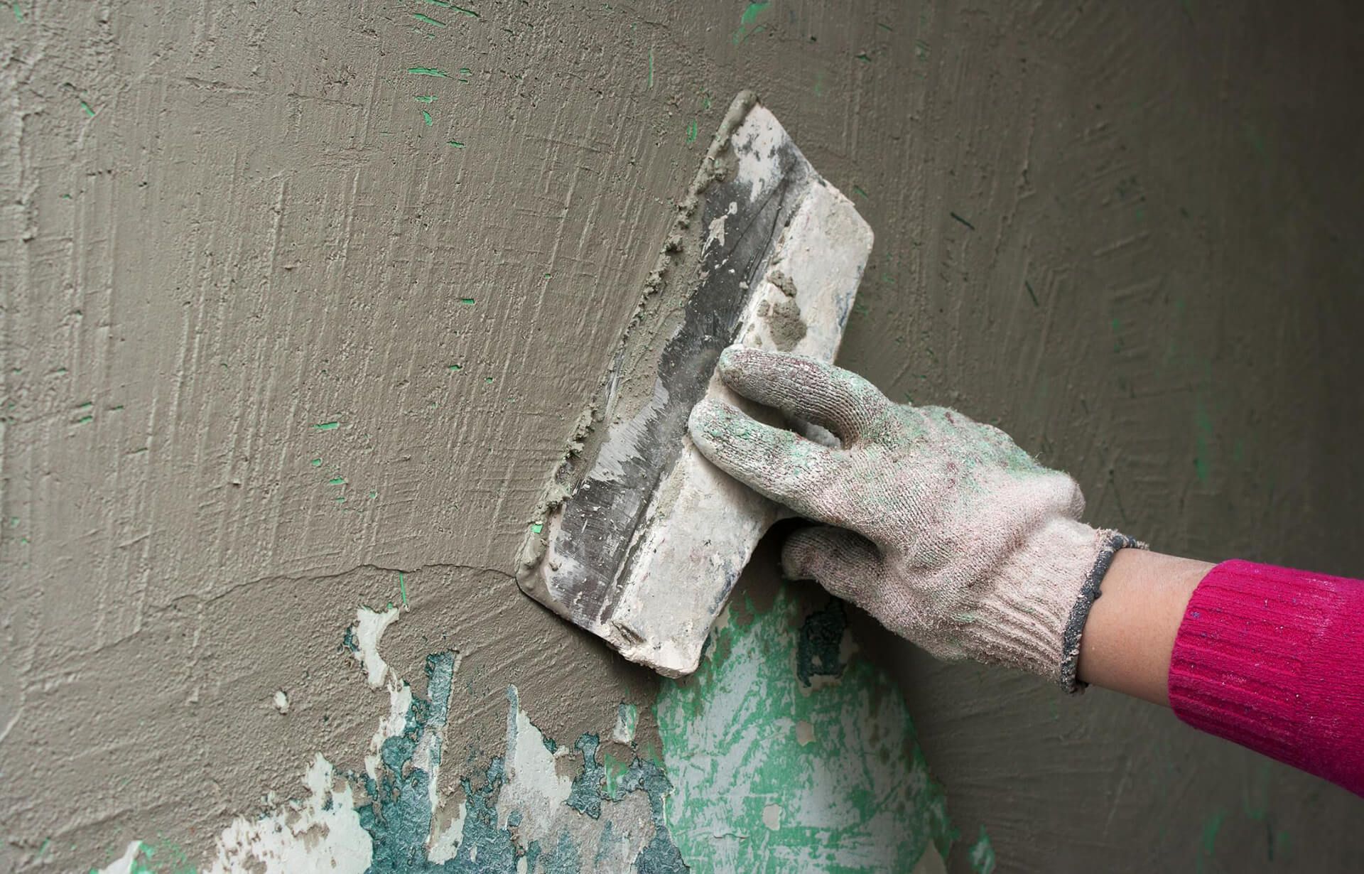 Person in work gloves smoothing plaster on a wall with a trowel.