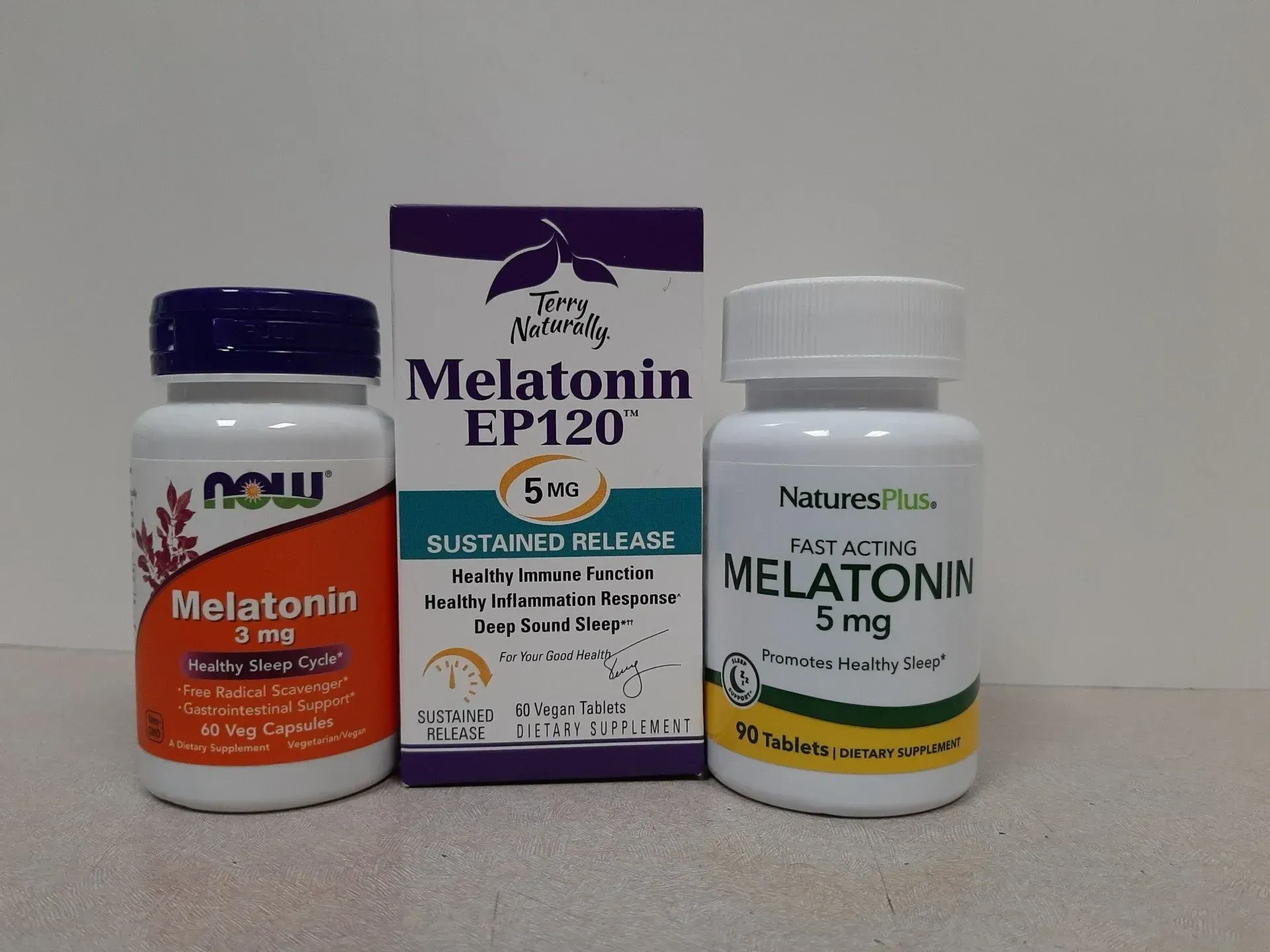 Three bottles and a box of 5mg melatonin supplements from Now, Time Matters, and NaturesPlus, displayed on a surface.