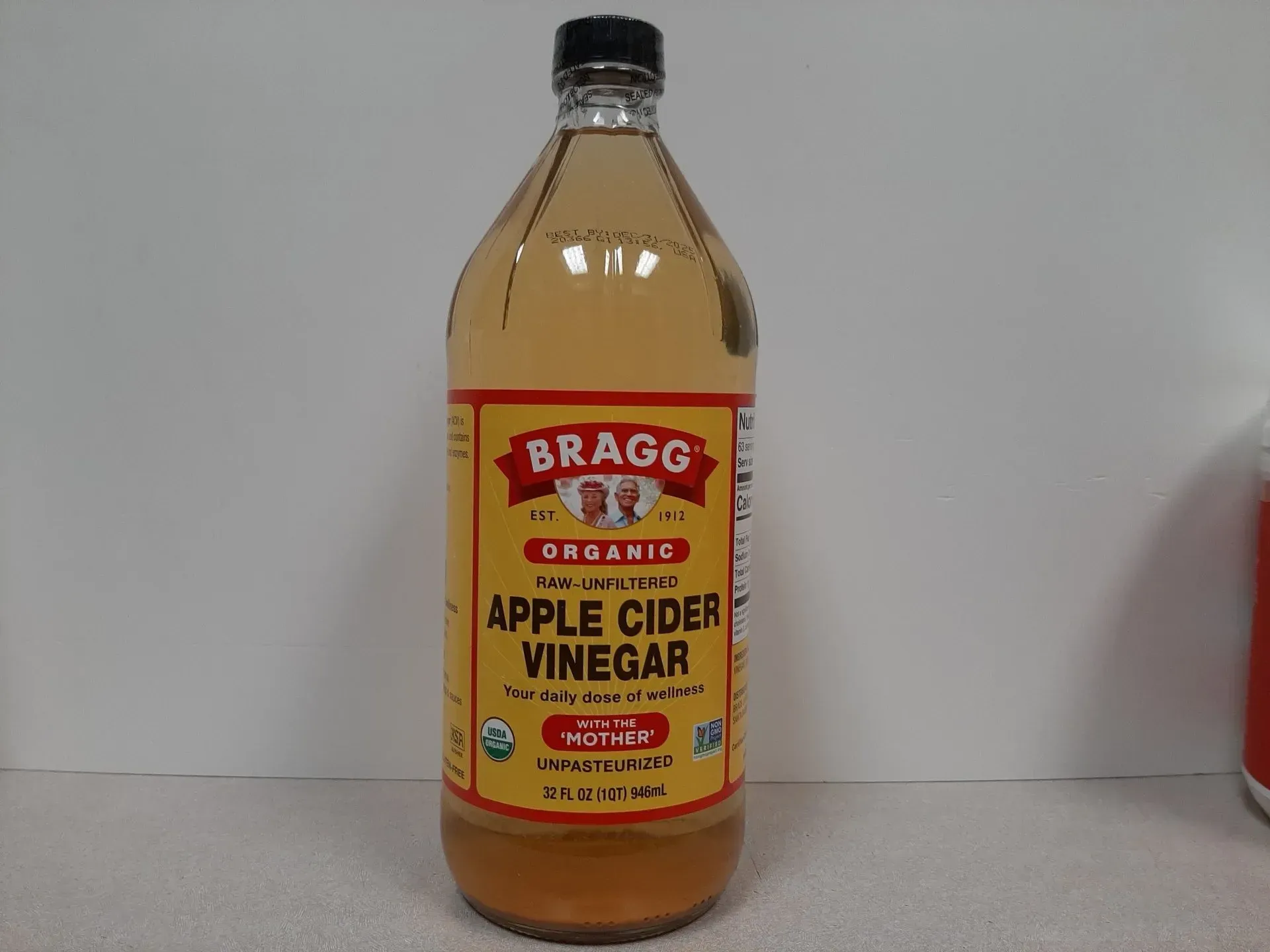 A bottle of Bragg Organic Raw Unfiltered Apple Cider Vinegar with a yellow label against a plain white background.