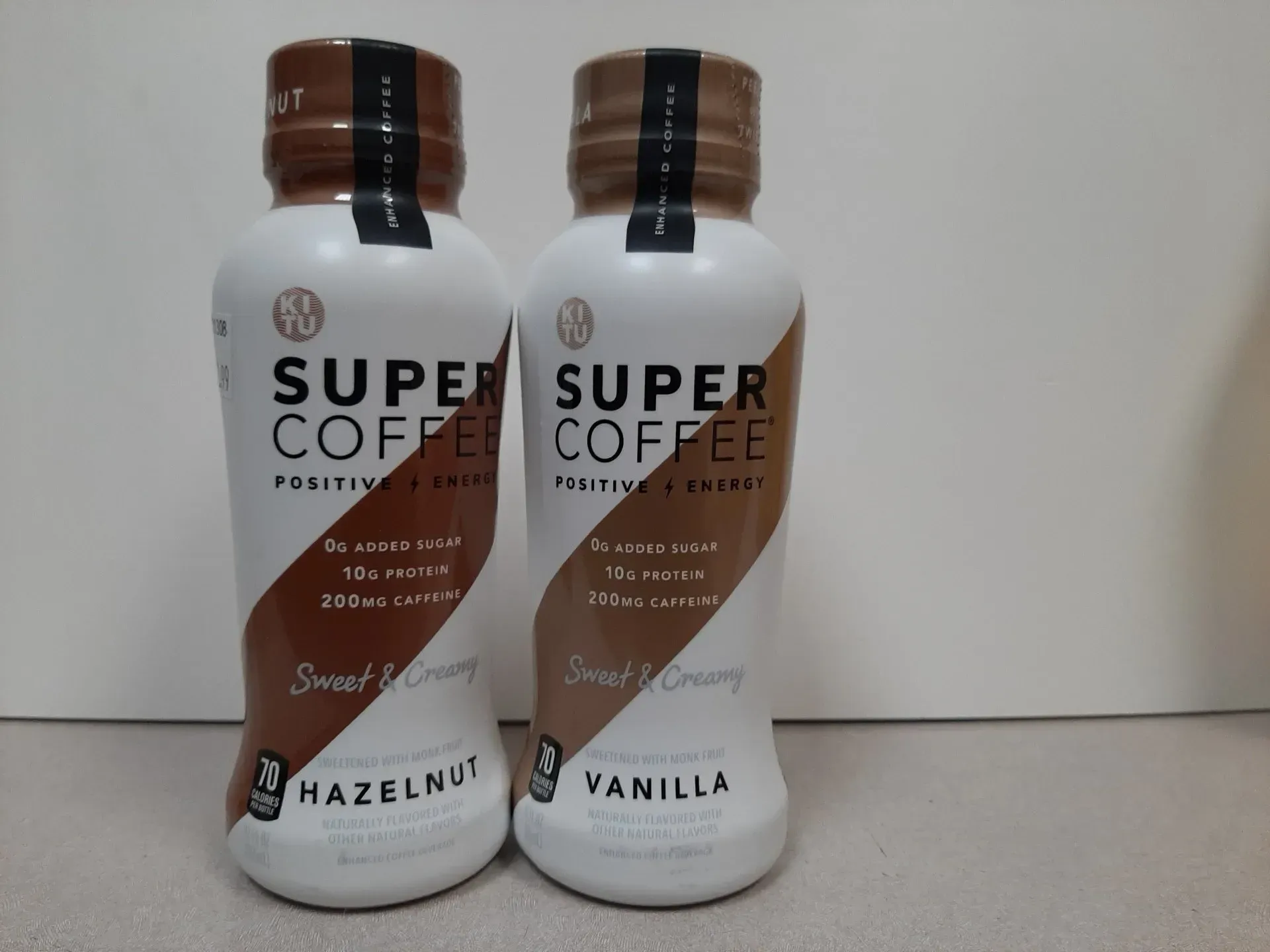 Two bottles of Super Coffee, flavors Hazelnut and Vanilla, standing side-by-side on a light-colored surface.